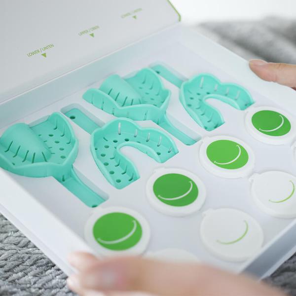 Zwei Hände halten eine geöffnete Box mit vier Zahnabdrucksets von SmileMeUp.